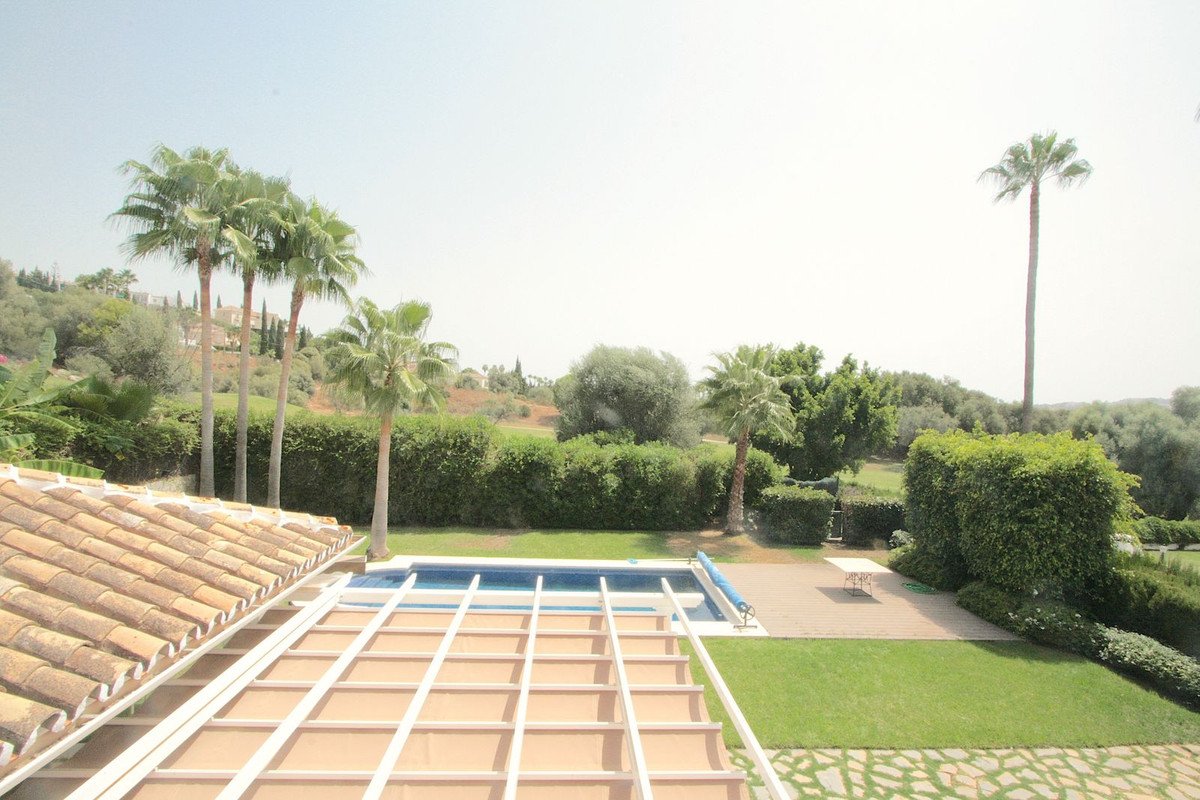 A residential outdoor space with a swimming pool, manicured hedges, palm trees, and green lawns under a bright sky.