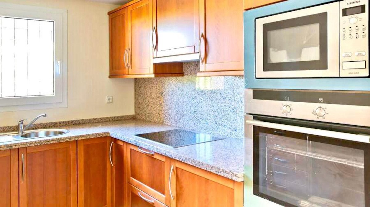 A modern kitchen featuring wooden cabinets, granite countertops, sink, induction hob, microwave, and oven.