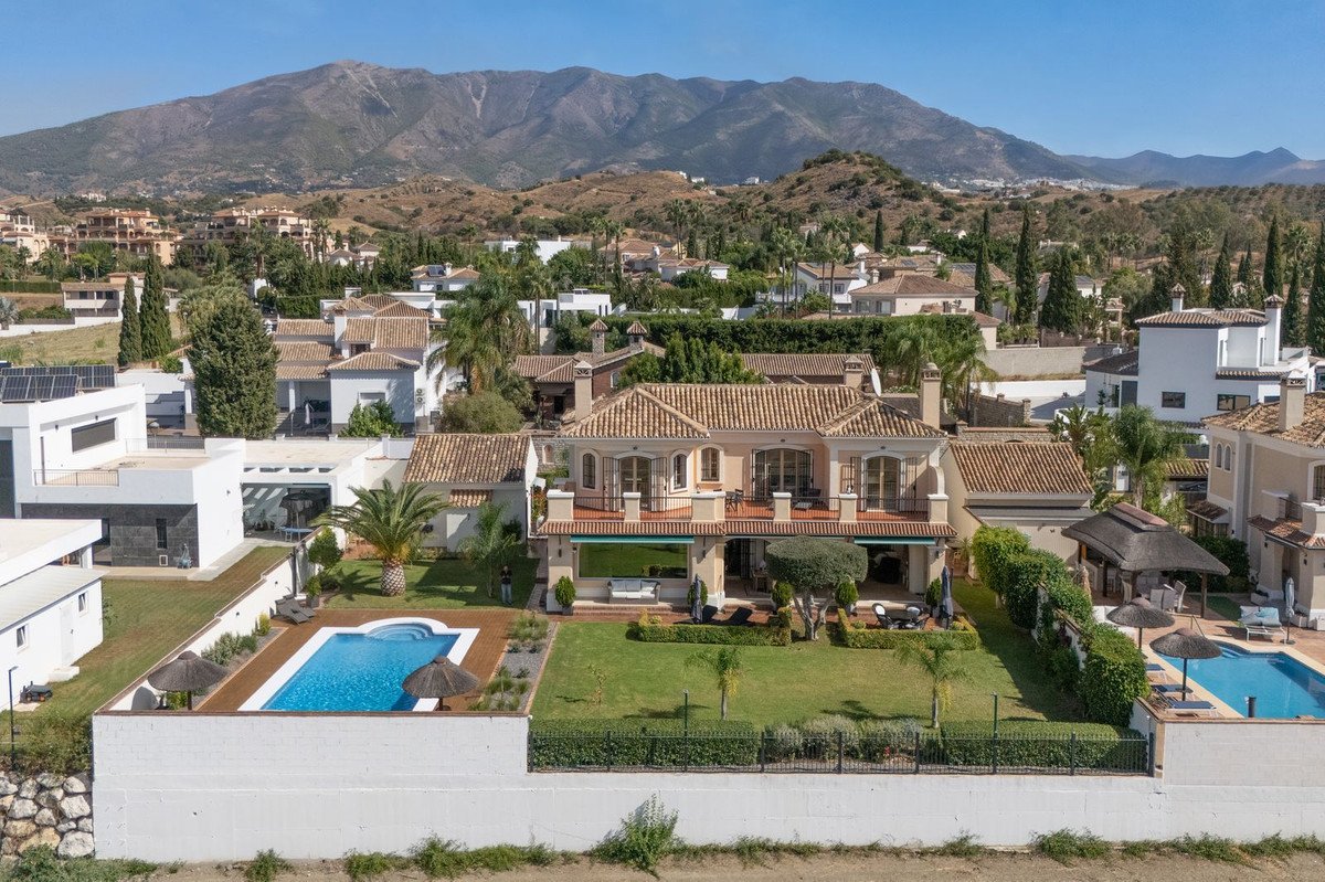 A luxury villa with a swimming pool, manicured gardens, and a mountain backdrop under a clear blue sky.