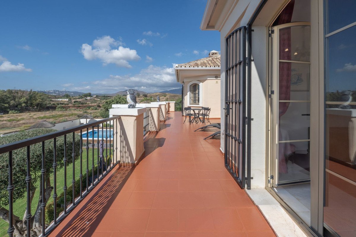 Spacious terrace with a view of a swimming pool and rolling hills under a blue sky.