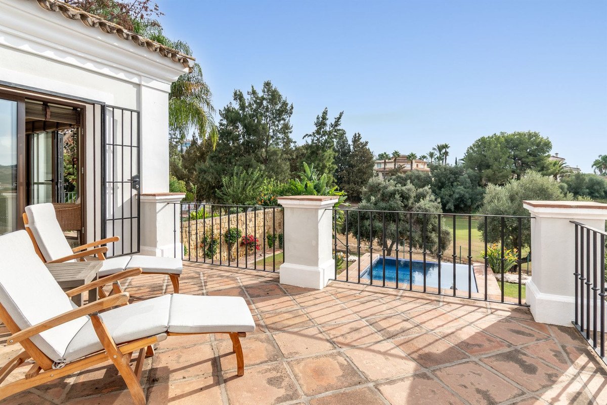 Terrace with lounge chairs overlooking a pool and lush greenery. Doors open to the interior.