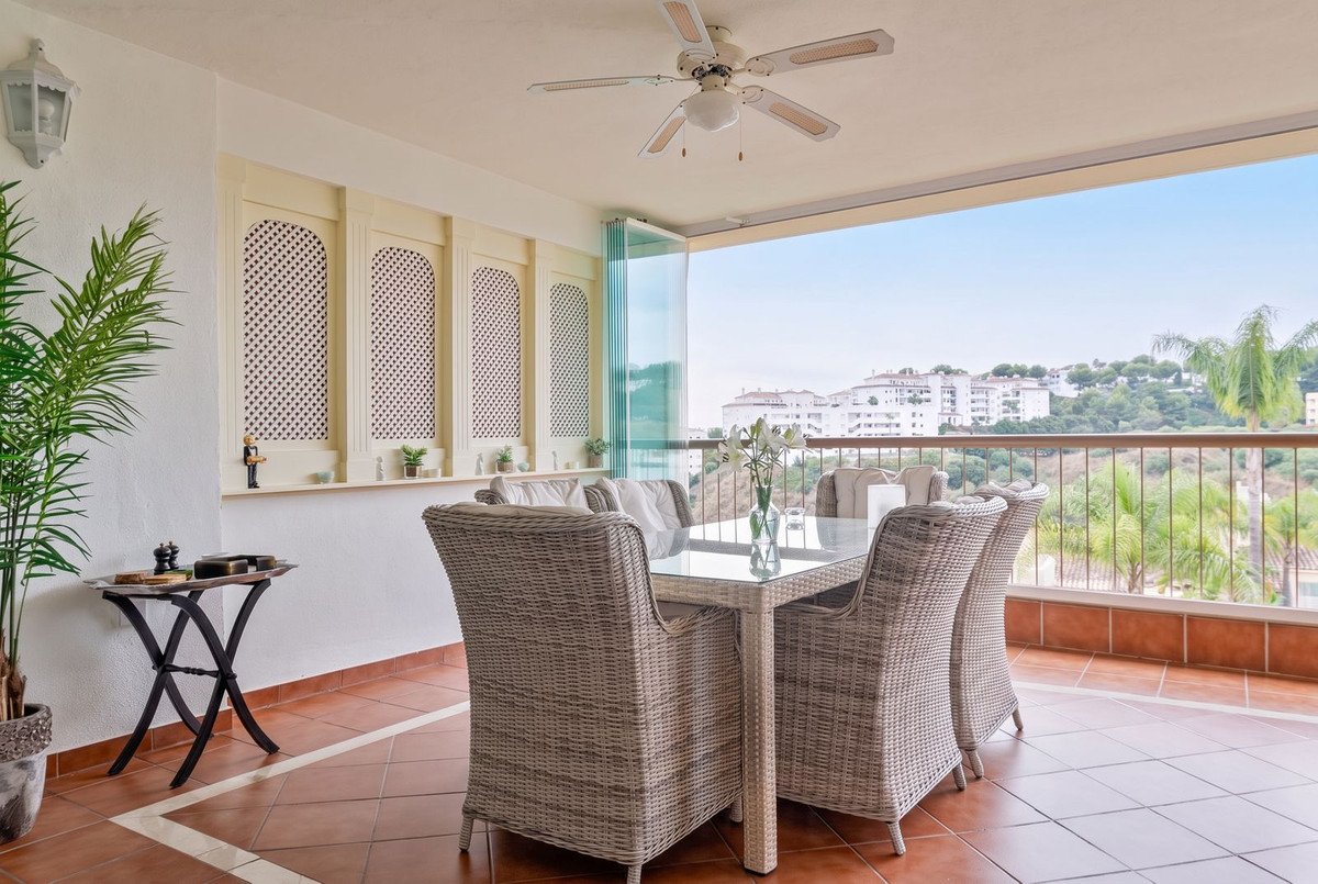 Outdoor dining terrace with wicker chairs, glass table, and city view