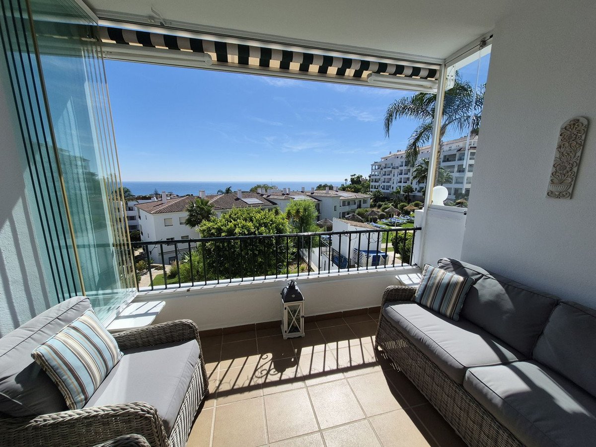 A covered balcony with comfortable seating offers a stunning sea view with surrounding buildings and greenery.