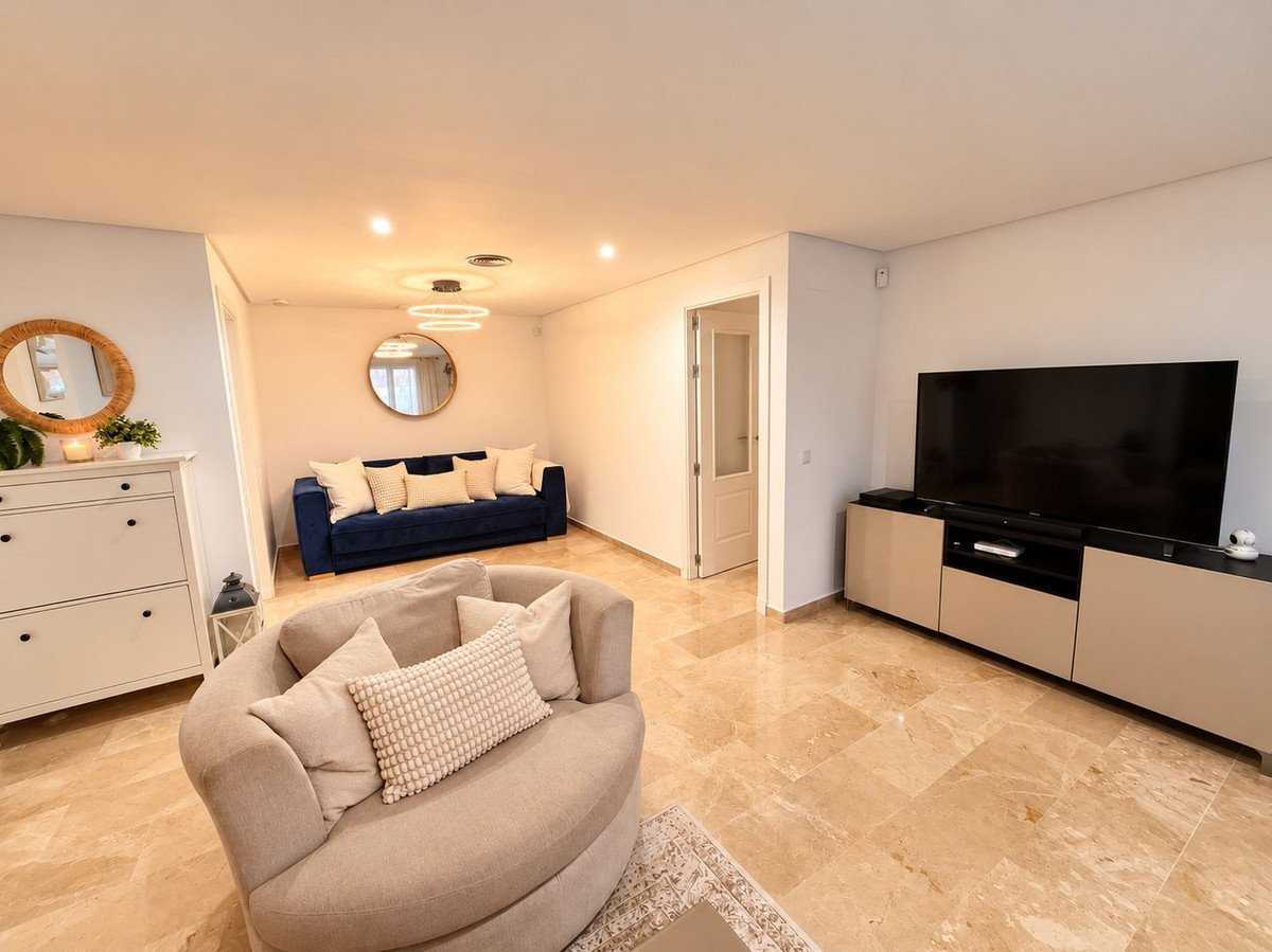 Modern living room with a blue sofa, comfortable armchair, large TV, and decorative mirrors on a marble floor.