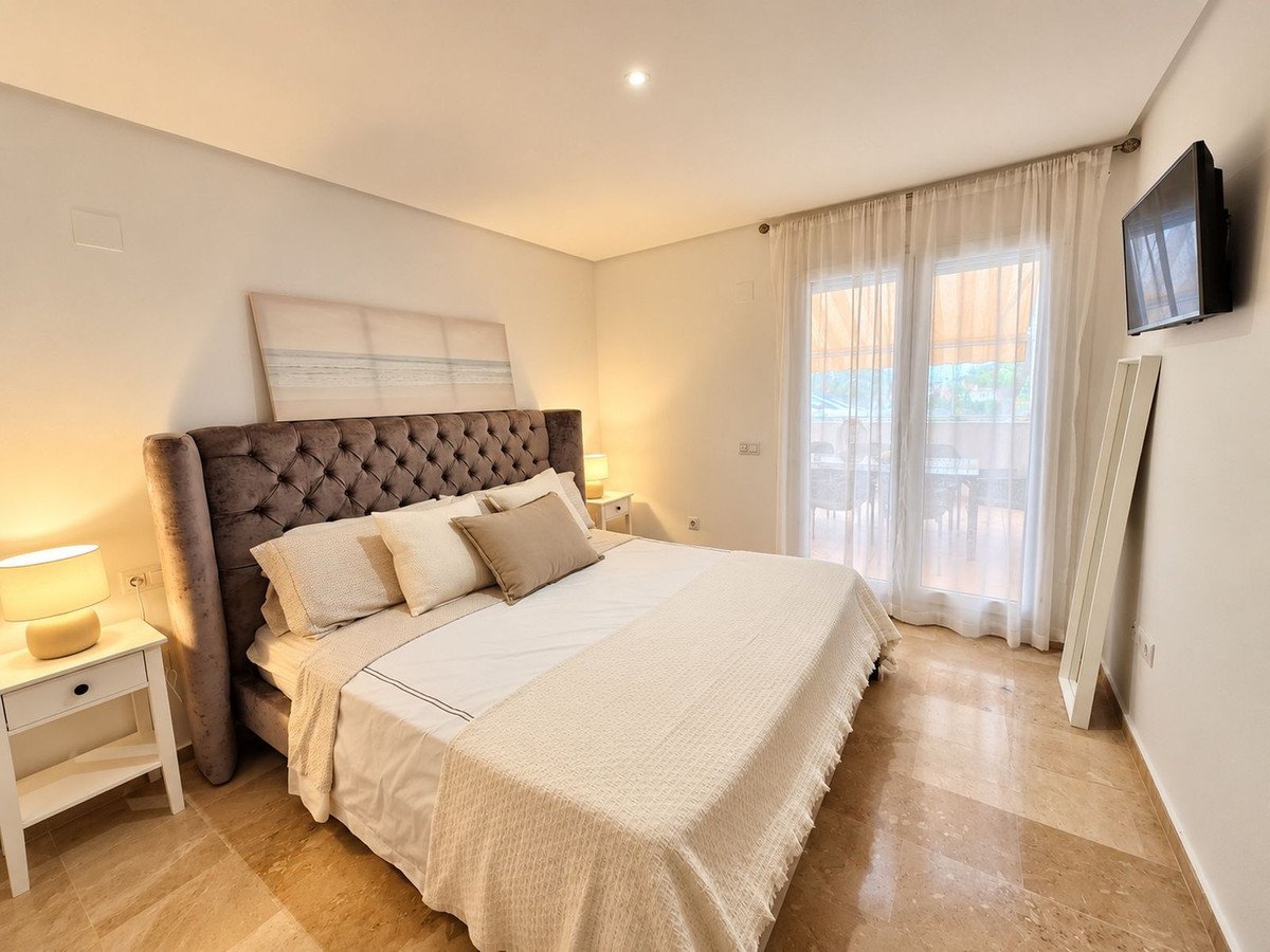 A spacious bedroom with a large bed, a tufted headboard, and a TV on the wall. French doors lead to a terrace.