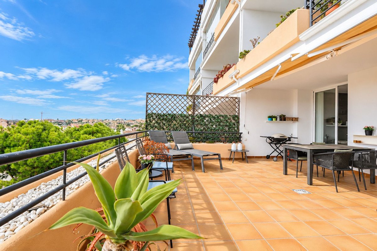 Spacious terrace with dining set, sun loungers, barbecue, and distant town views under a clear blue sky.
