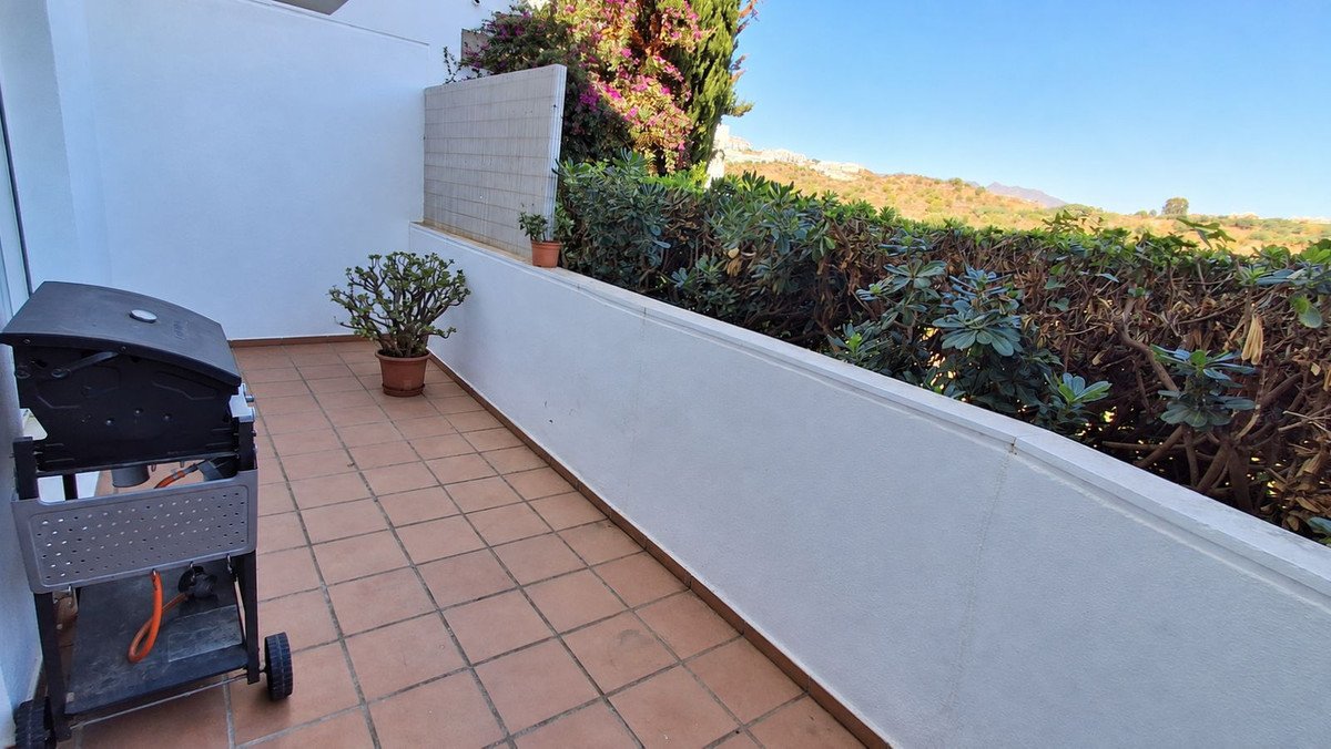 Tiled terrace with a barbecue grill and a potted plant, offering a view of lush greenery and distant hills.