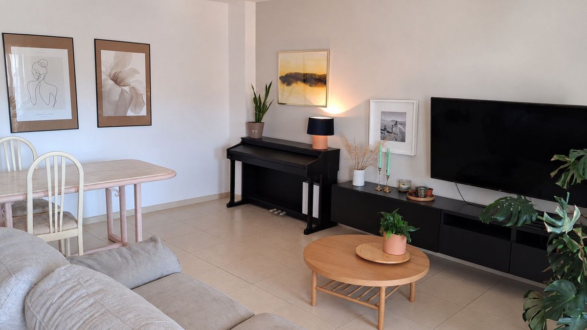 A living area with a digital piano, dining table, sofa, and TV, decorated with framed art and plants.