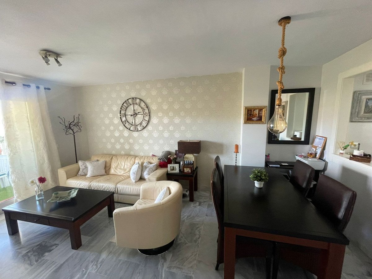A bright living and dining area featuring a cream sofa, armchair, dining table, and decorative clock on a patterned wall.