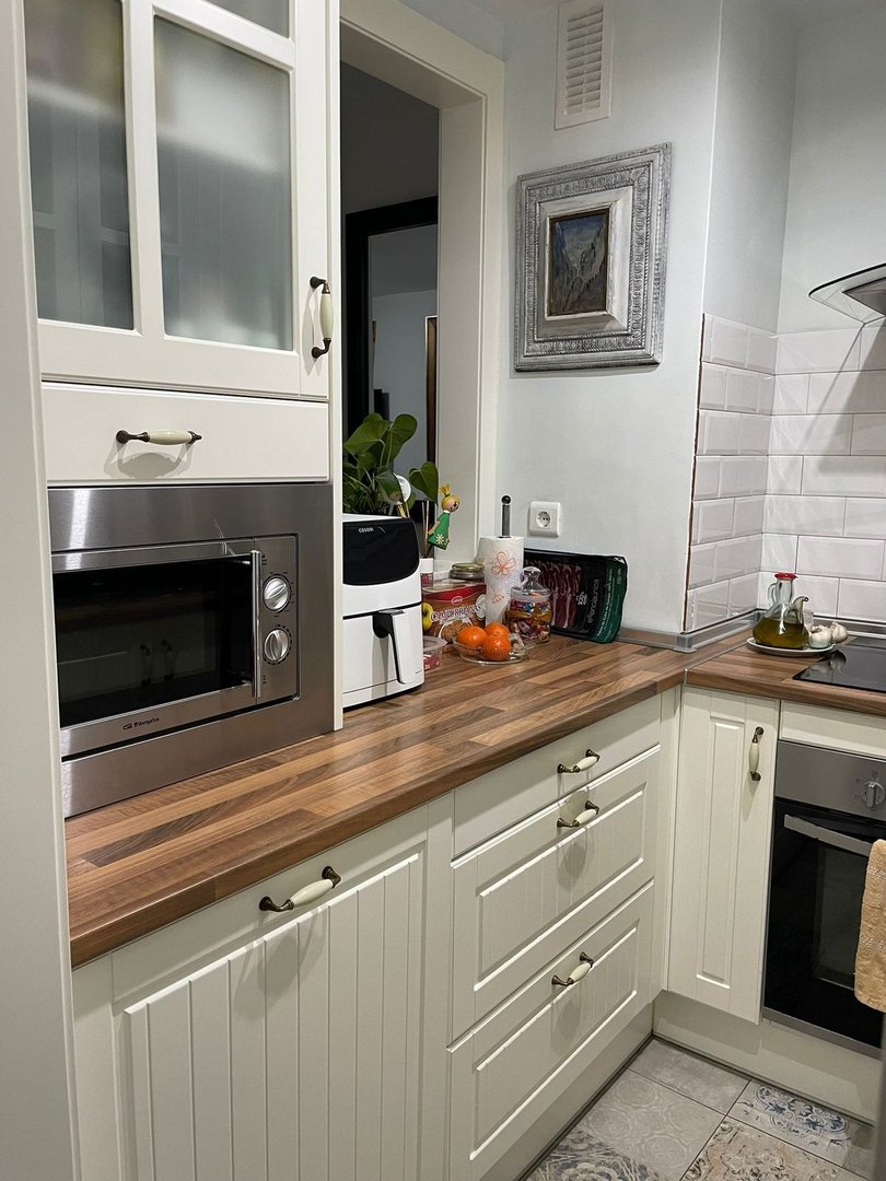 Modern kitchen with cream cabinetry, wooden countertops, stainless steel microwave, and oven. White subway tile backsplash.
