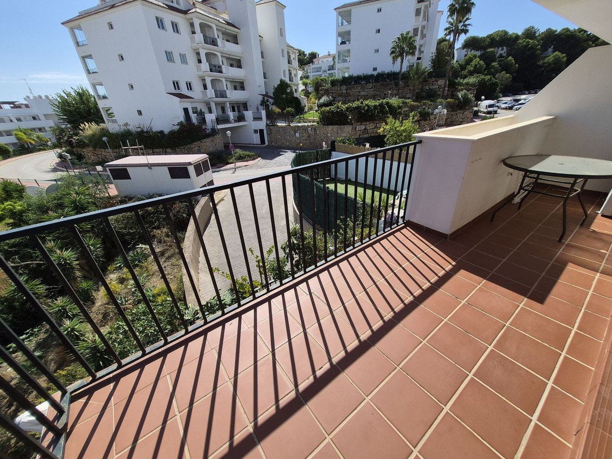 Balcony with terracotta tiles, black railing, and view of apartment buildings and greenery