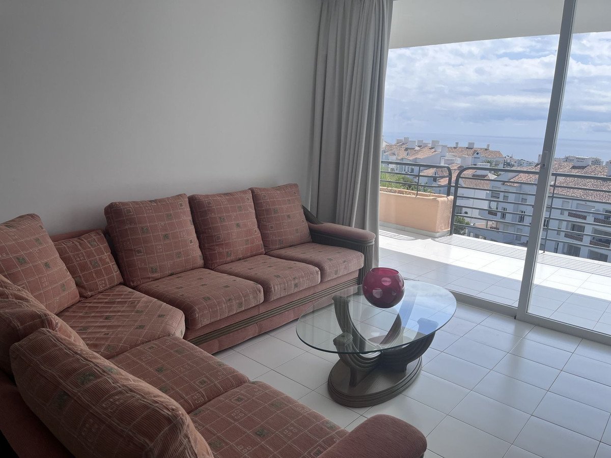 A sectional sofa in a living room with a balcony overlooking a coastal town and the sea.