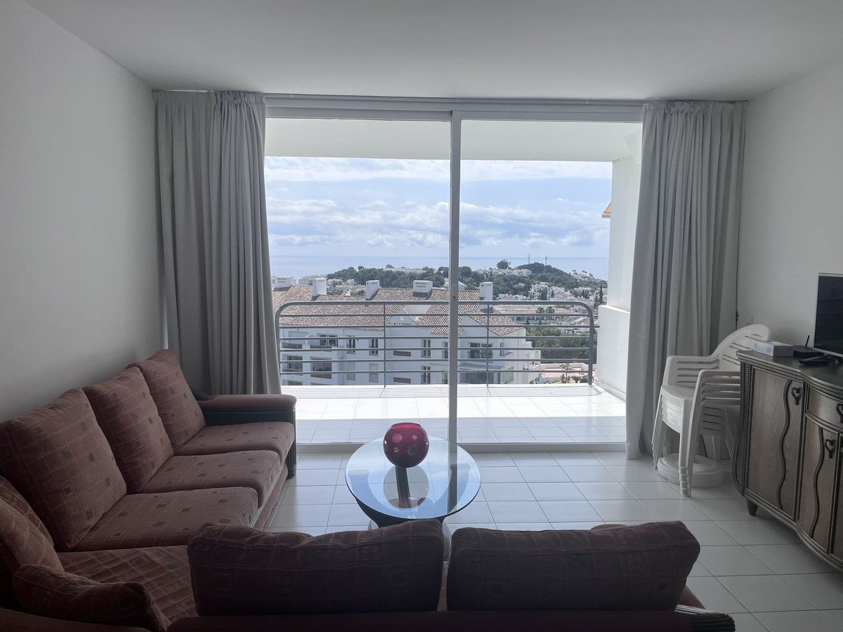 Living room with a large window offering a view of the sea, balcony, and surrounding buildings.