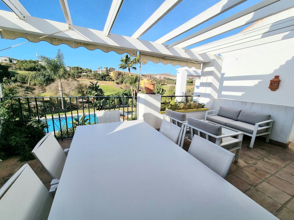Covered terrace with dining table and sofas overlooking a swimming pool and landscaped gardens.