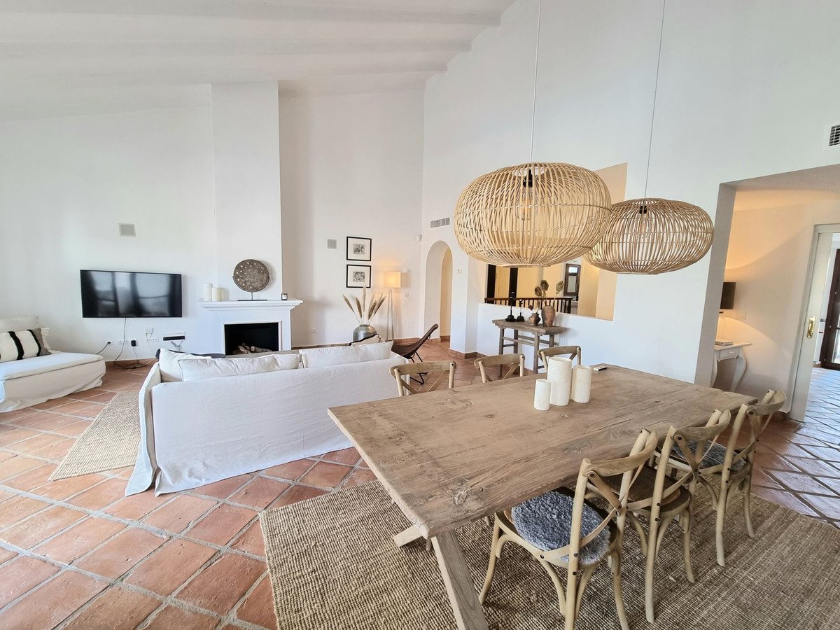 Spacious living and dining area with a fireplace, comfortable sofas, a large wooden table, and unique woven pendant lights.