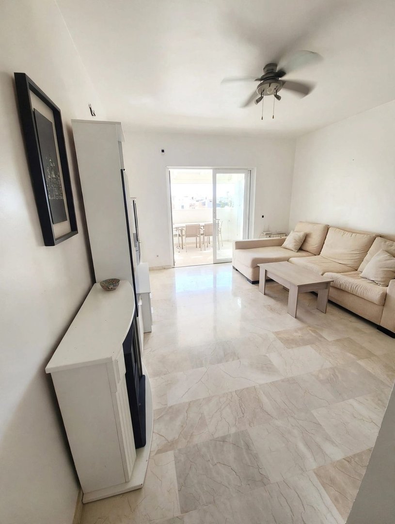 A bright living room with a large sofa, coffee table, and sliding doors leading to an outdoor patio with a table and chairs.