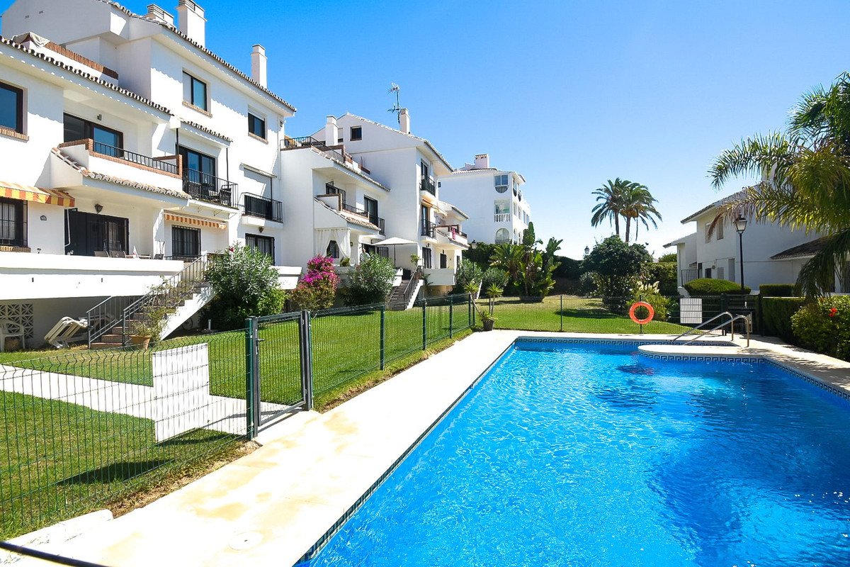Apartment buildings with balconies overlooking a sunny courtyard and a vibrant blue swimming pool with a green lawn.