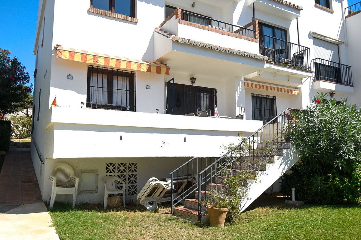 Exterior view of a white apartment building with balconies, awnings, and a lawn with stairs leading up.