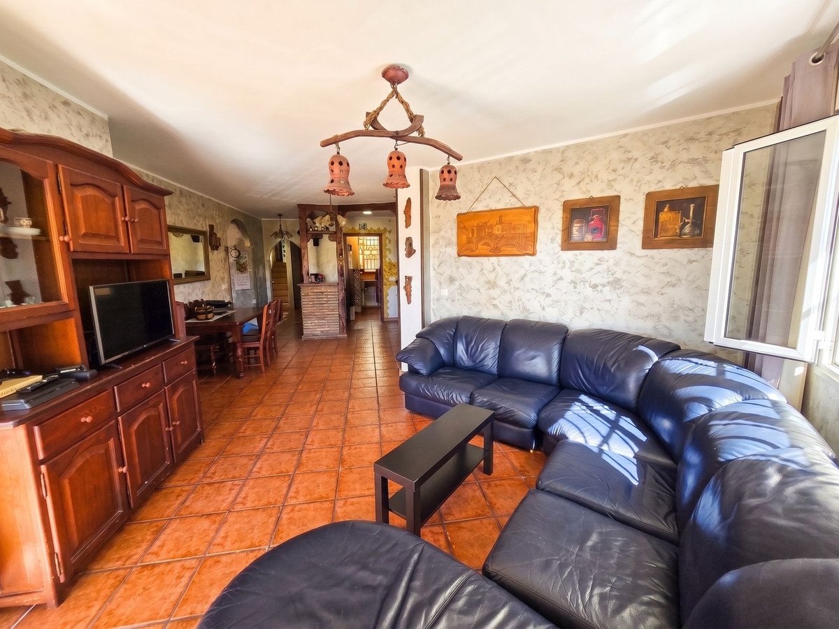 Spacious living room with a dark leather sectional sofa, TV, wooden cabinet, and a view into the dining area.
