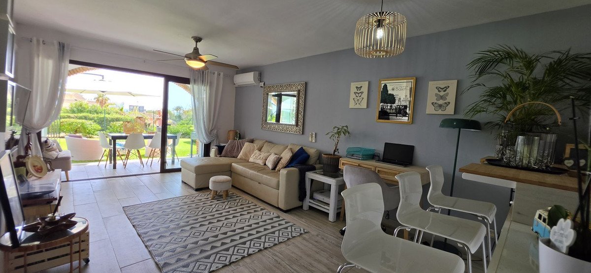 Living room with L-shaped sofa, desk, and large sliding doors opening to a garden terrace with dining table.