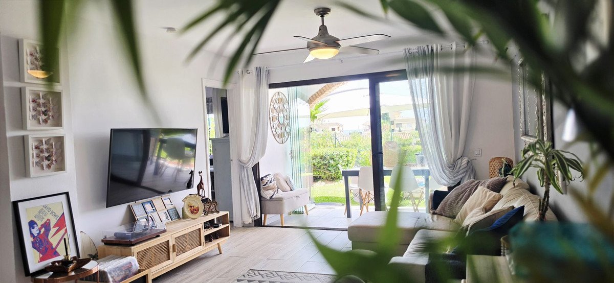 Modern living room with a comfortable sofa, TV, and a view of a green garden through glass sliding glass doors.