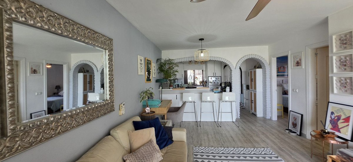 Open-plan living area with a sofa, dining table, kitchen bar with stools, and a view into bedrooms through archways.