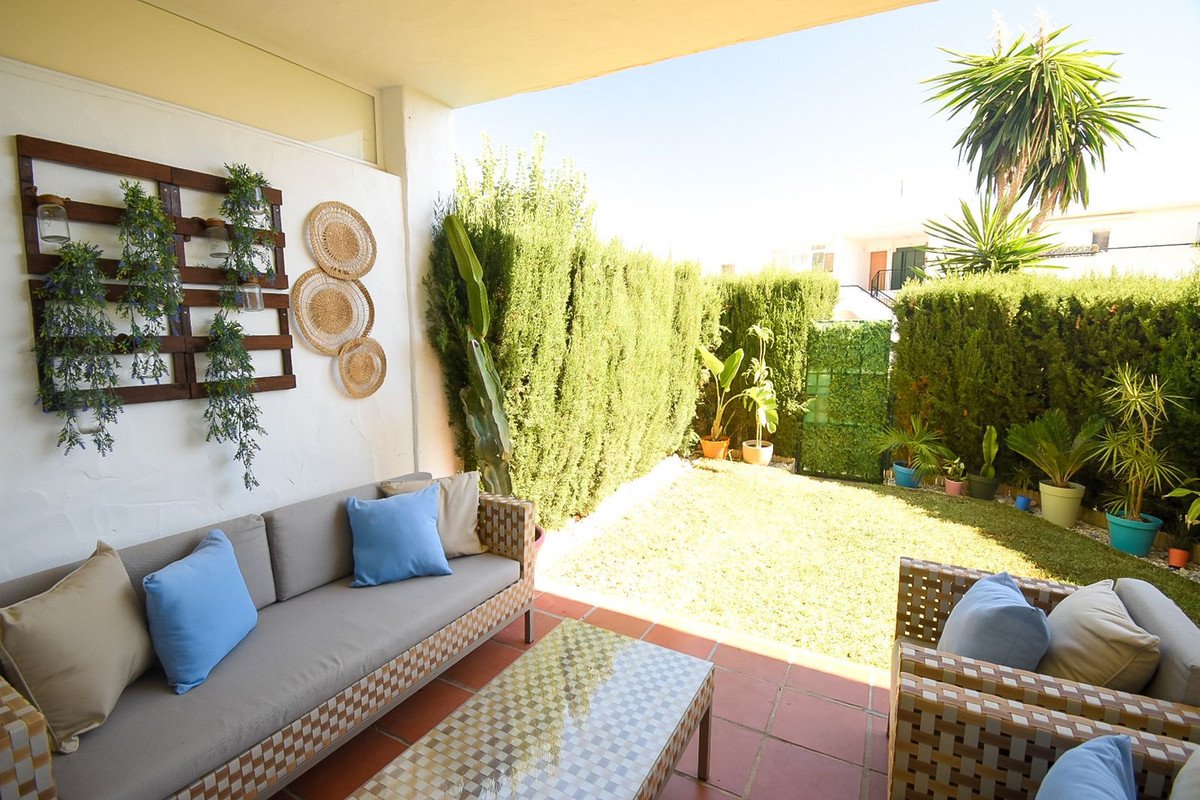 Terrace with outdoor seating, a lush green garden, and a palm tree under a sunny sky.