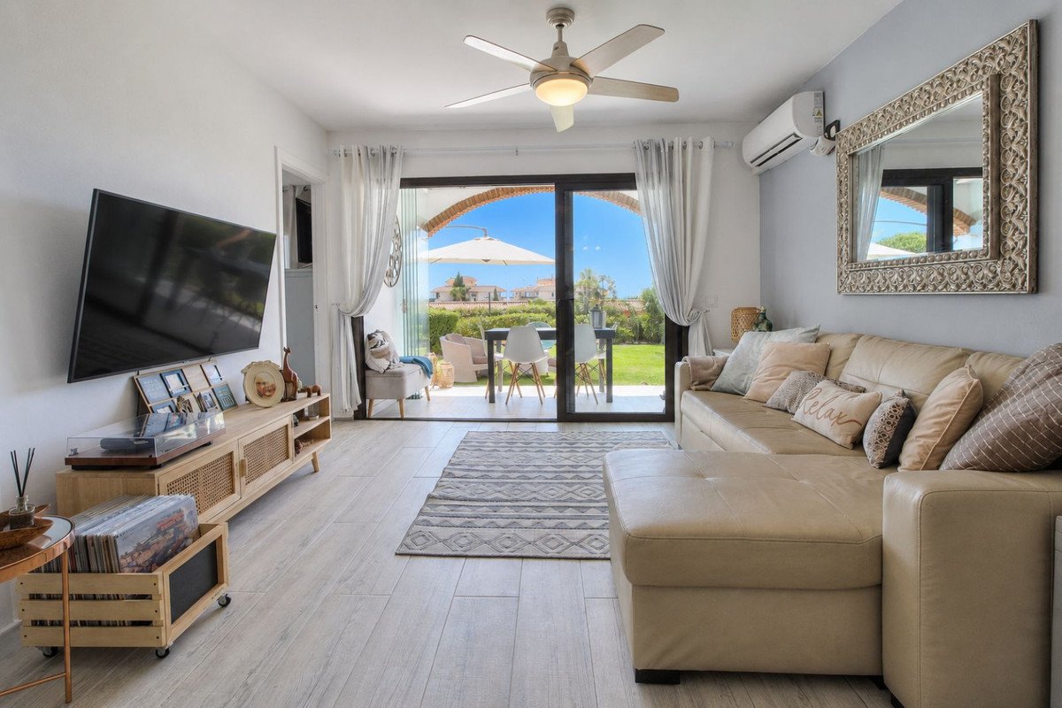 Modern living room with a sectional sofa, TV, and sliding glass doors opening to a garden patio with outdoor seating.
