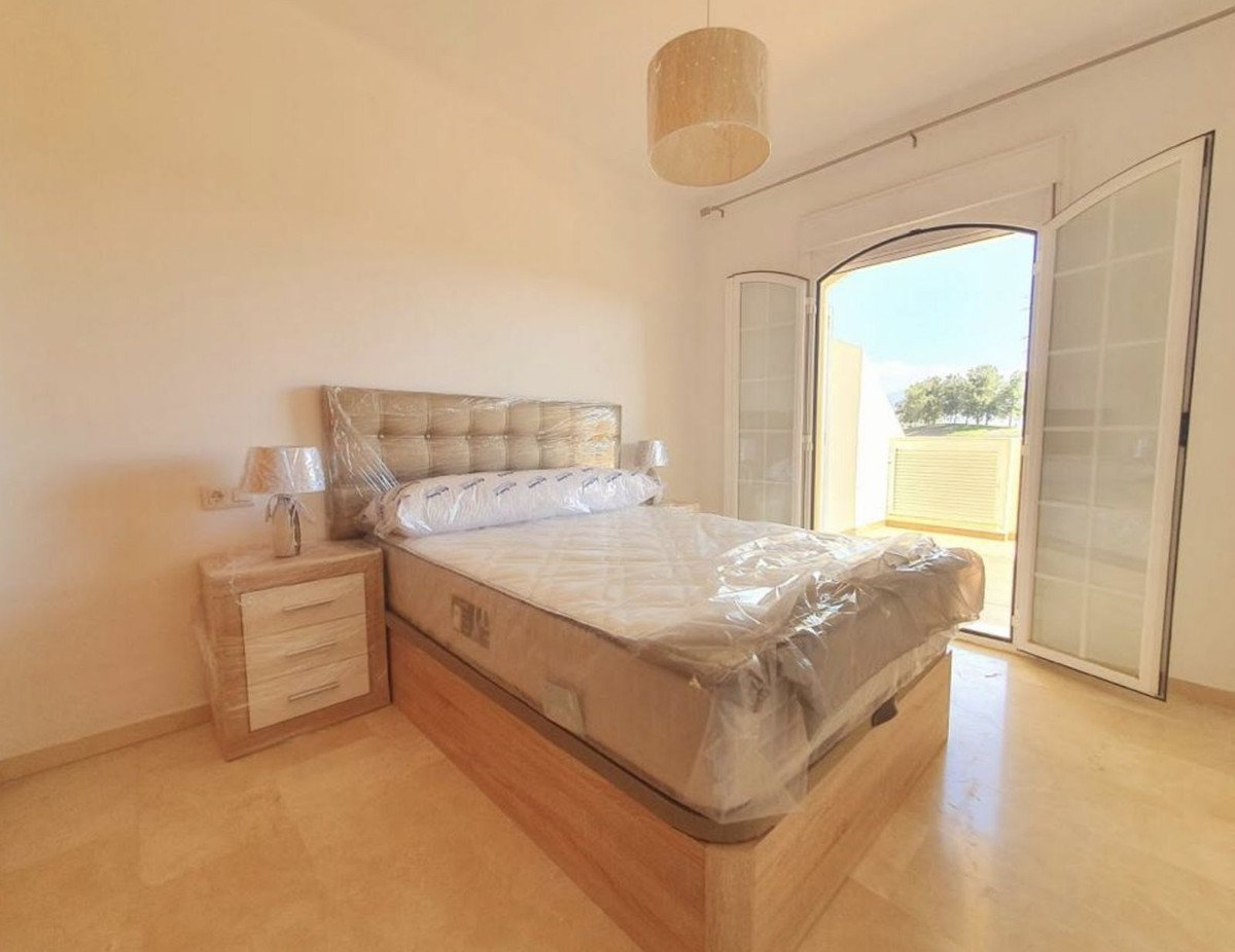 A bedroom with a bed, nightstand, and a balcony door opening to a view of trees and a sunny day.