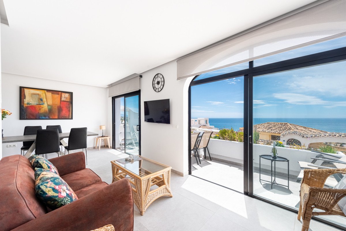 Bright living and dining area with a large window showcasing a beautiful sea view and access to a balcony with outdoor seating.
