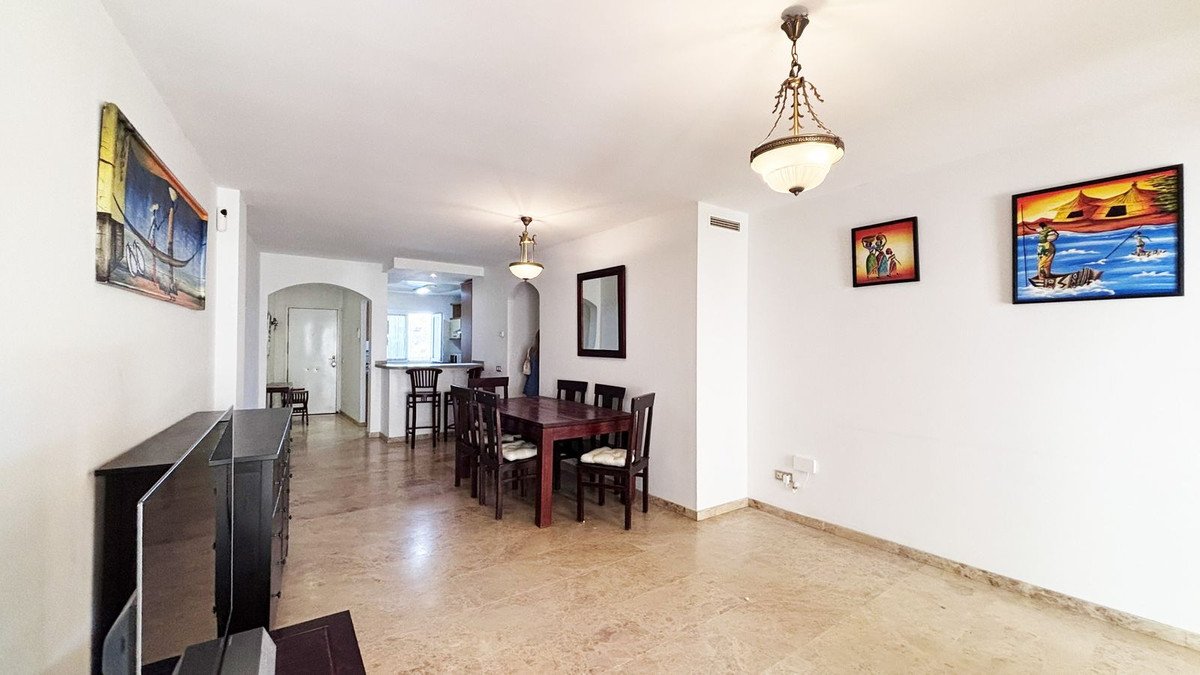 Spacious open-plan living and dining area with a wooden table, chairs, and bar stools, decorated with paintings.