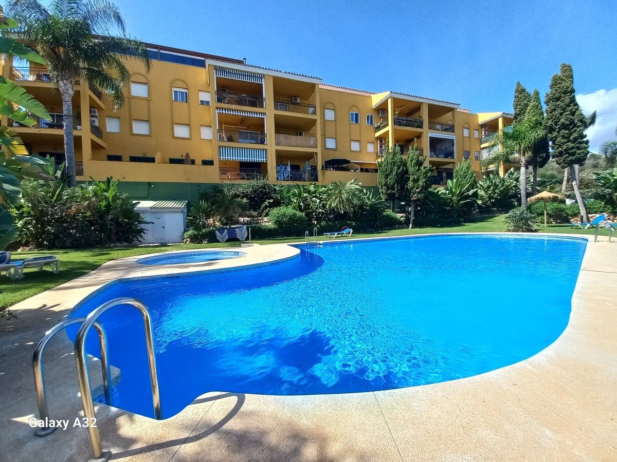 Outdoor swimming pool and hot tub area in front of a yellow apartment building with balconies and lush greenery.