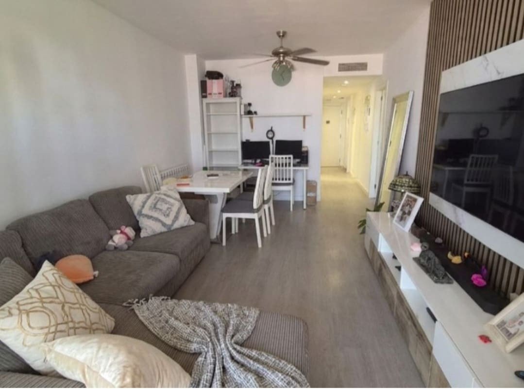 A modern living and dining area with a sofa, dining table, and a workspace with two computer monitors on a desk.