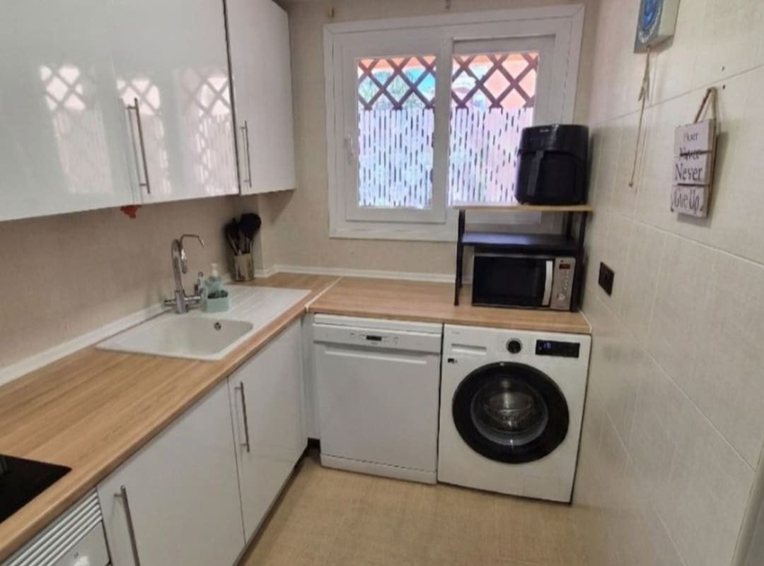 Modern white kitchen with wooden countertops, sink, dishwasher, washing machine, microwave, and air fryer.