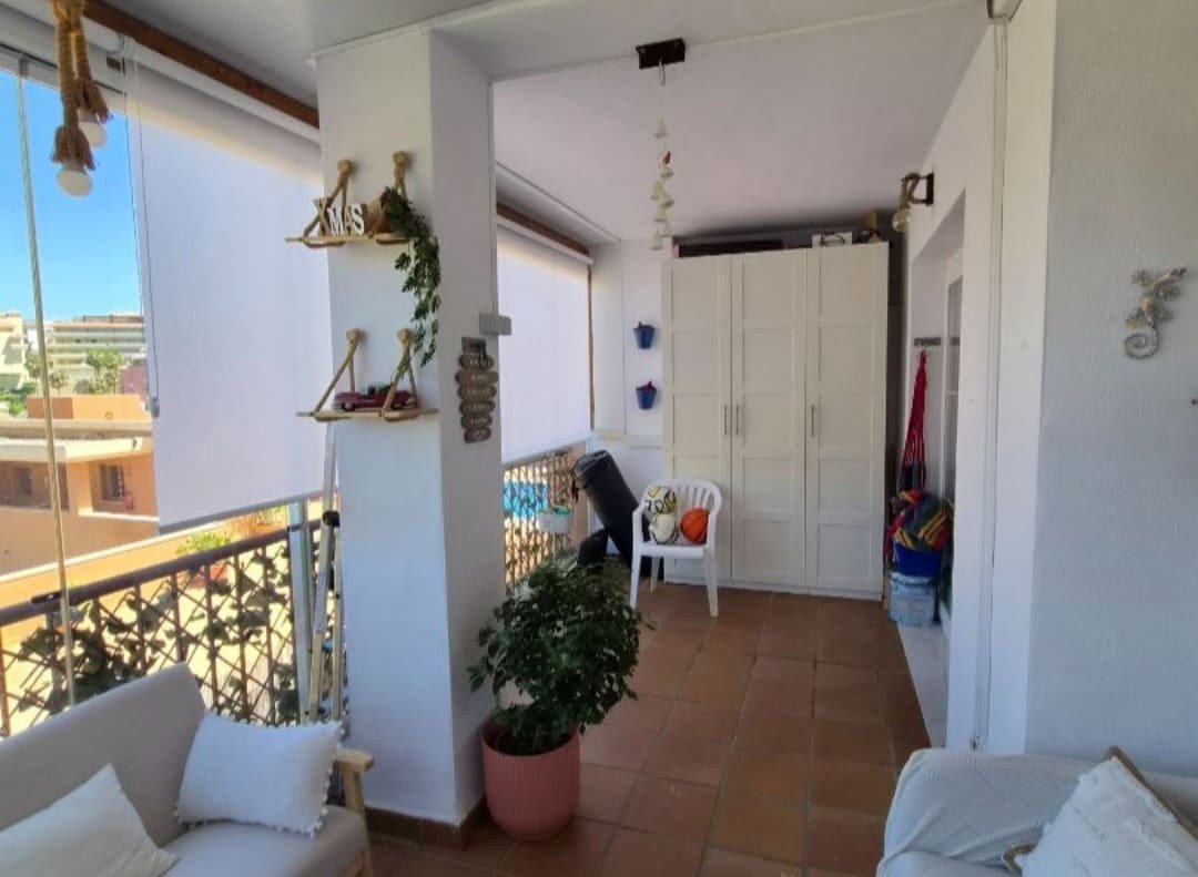 Covered balcony with a sofa, white wardrobe, plant, and views of buildings and sky.