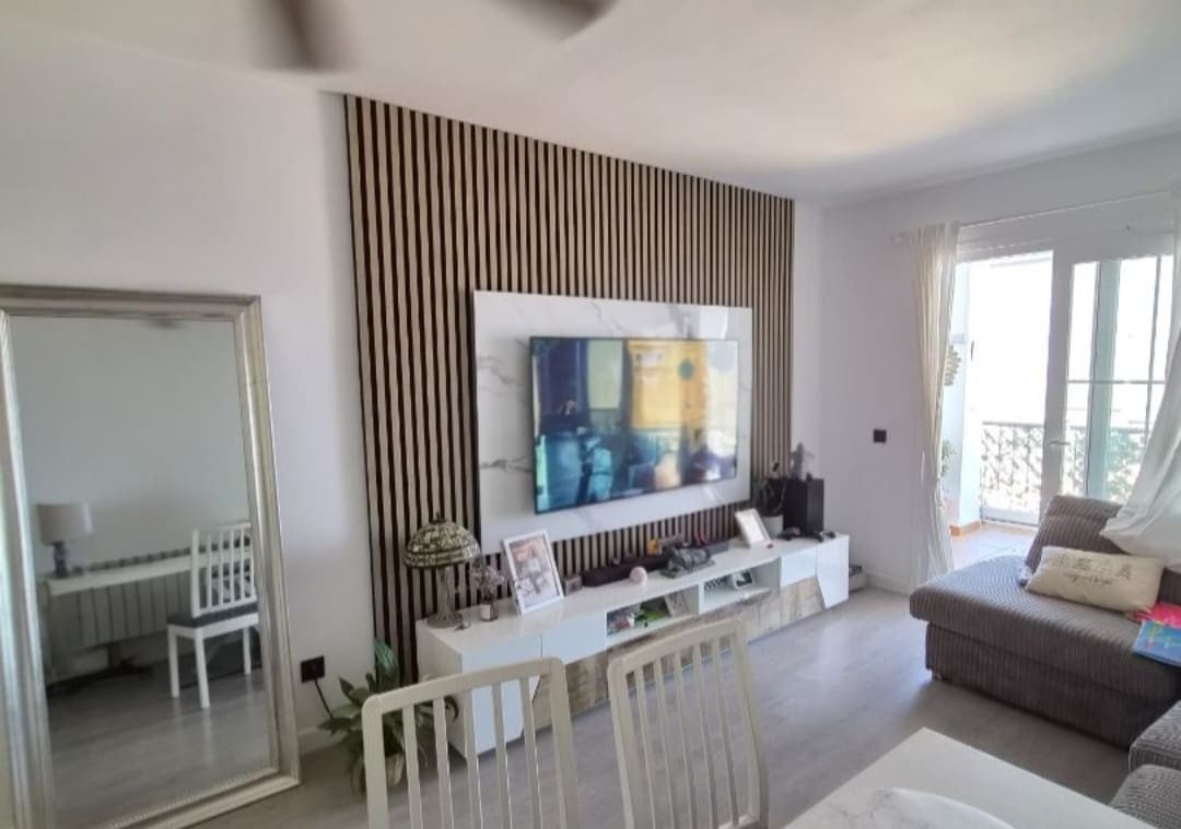 Modern living room with a large TV mounted on a slatted wall, a sofa, and a balcony view.