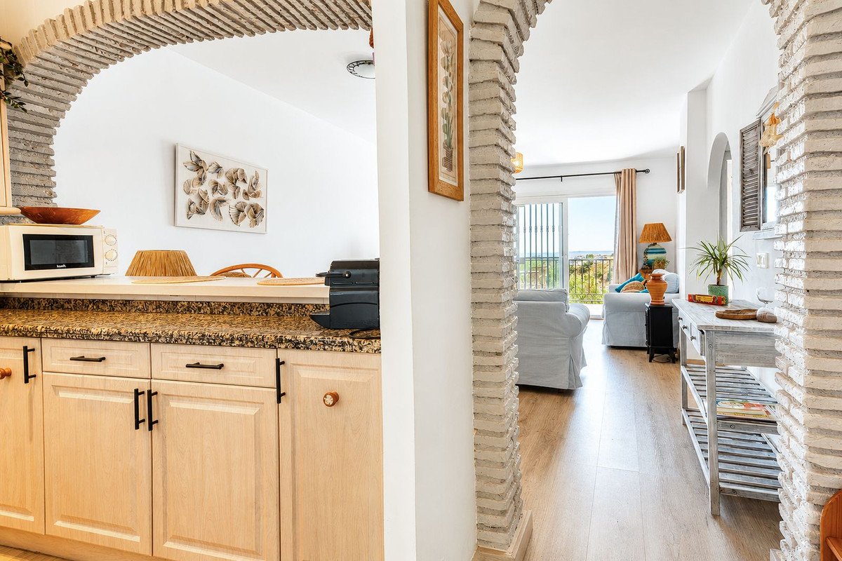 Kitchen area with microwave and cabinets, opening to a living room with sofas and a balcony offering a sea view.