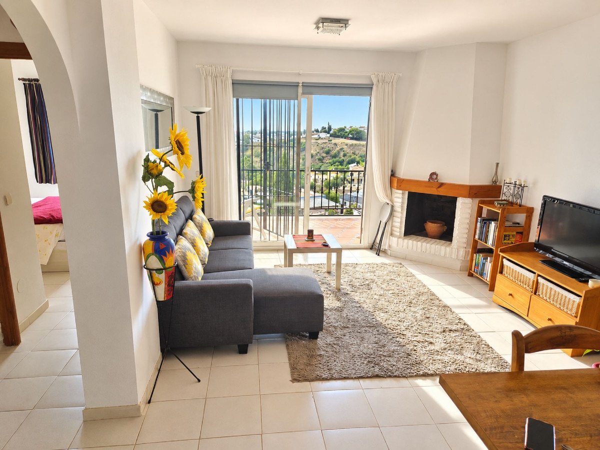 A spacious living room with a grey sectional sofa, fireplace, television, and a balcony with a scenic view.