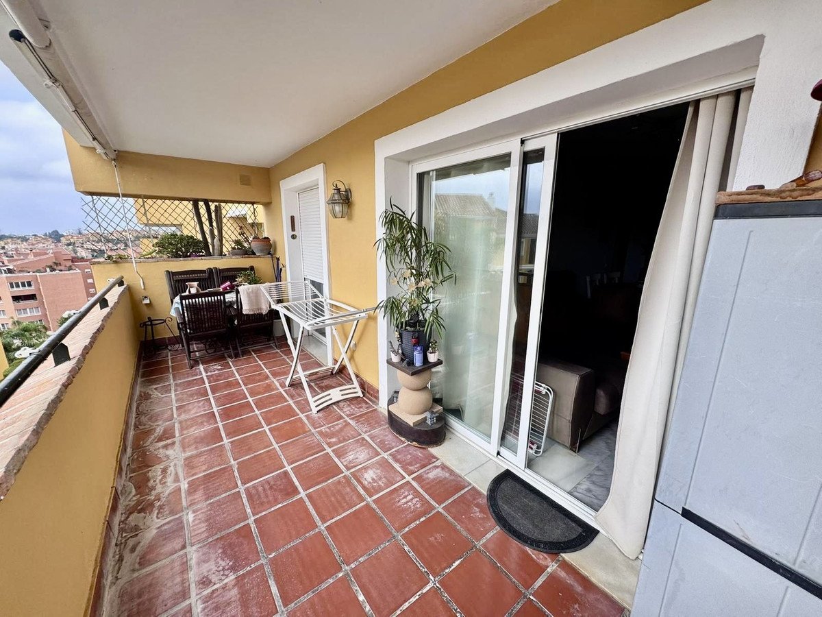 A balcony with red tiled flooring, outdoor seating, a drying rack, and a view of buildings and trees.