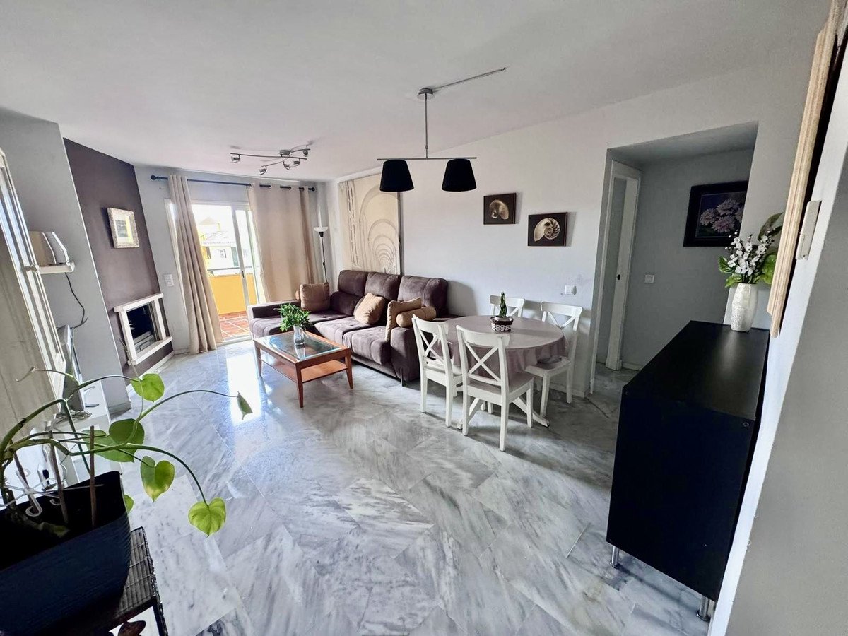 Bright living and dining area with a sofa, dining table, fireplace, and balcony access.