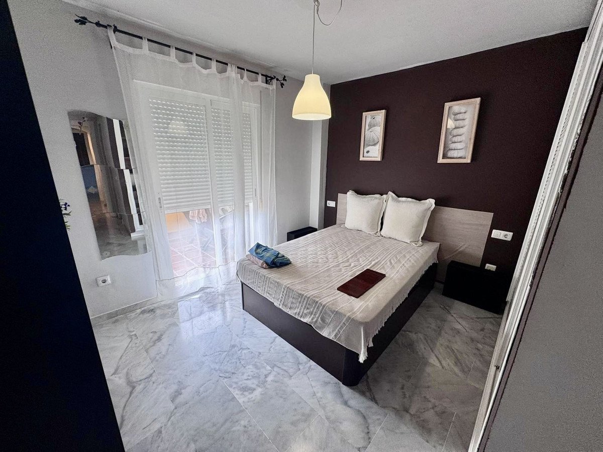 A well-lit bedroom featuring a king-size bed, bedside tables, a large mirror, and large windows with sheer curtains.