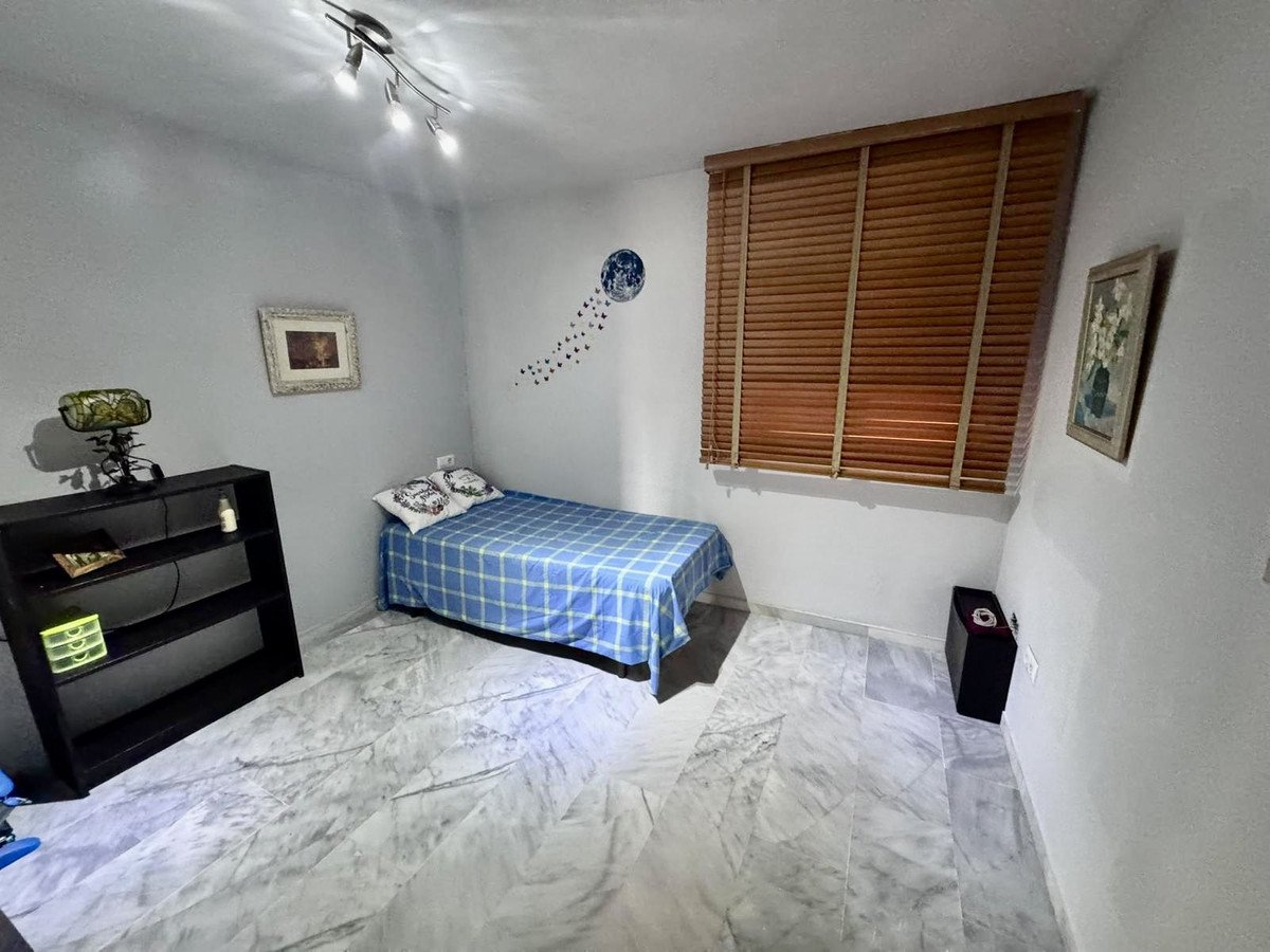 A bedroom with a single bed covered in blue plaid bedding, a black bookshelf, and wooden blinds covering the window.
