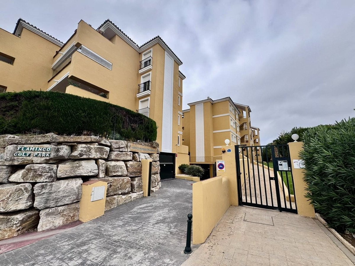 Flamingo Golf Park gated entrance with yellow apartment buildings and stone wall in the foreground.
