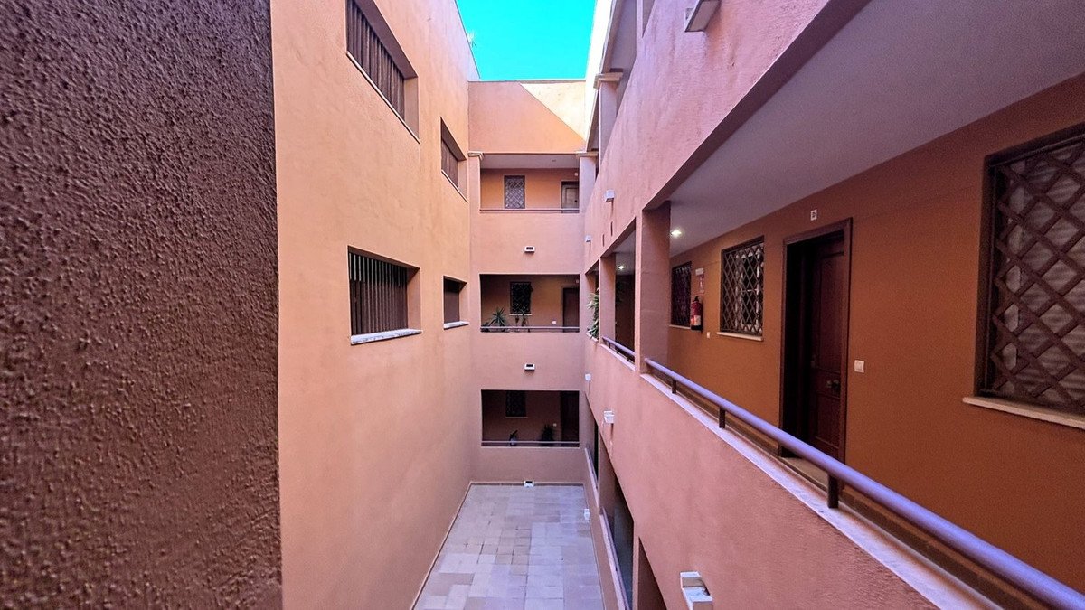 Exterior view of a courtyard with balconies, doors, and windows, under a clear blue sky.