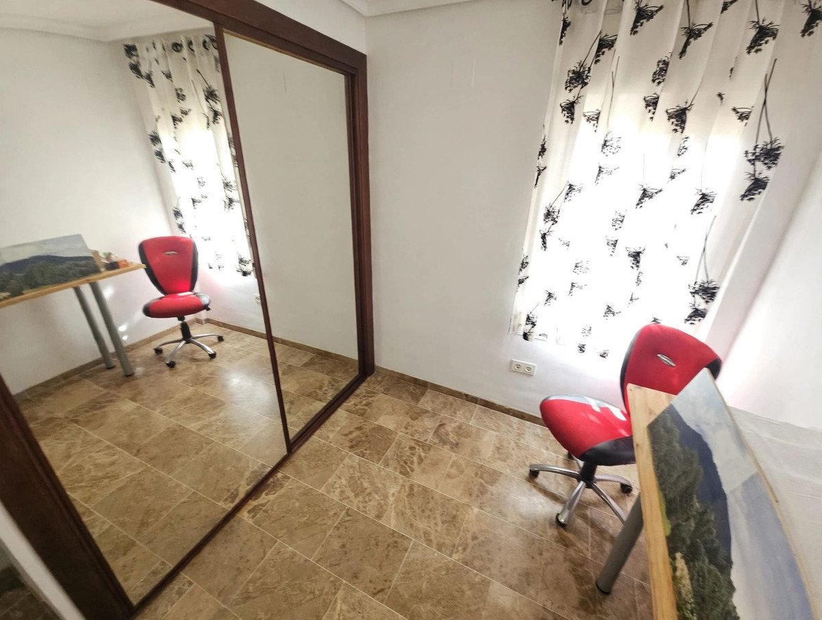 A red office chair is next to a desk, reflected in a large mirrored closet door. Curtains hang by the window.
