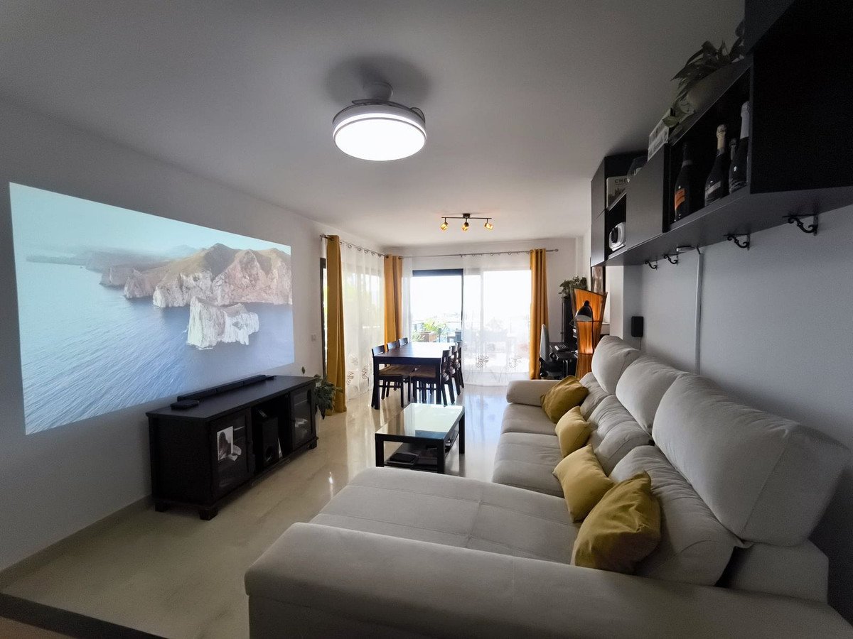 Spacious living room with large sectional sofa, projector screen displaying a sea view, dining area, and balcony access.