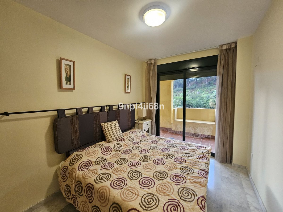 Bedroom with a patterned bed, large window overlooking a balcony with green hillside views and trees.