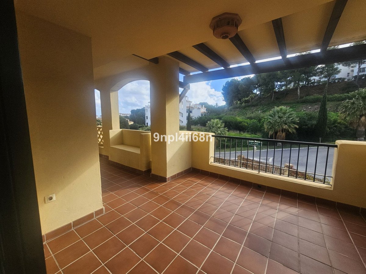 Spacious tiled terrace with a built-in bench and a railing overlooking a green hillside and trees.