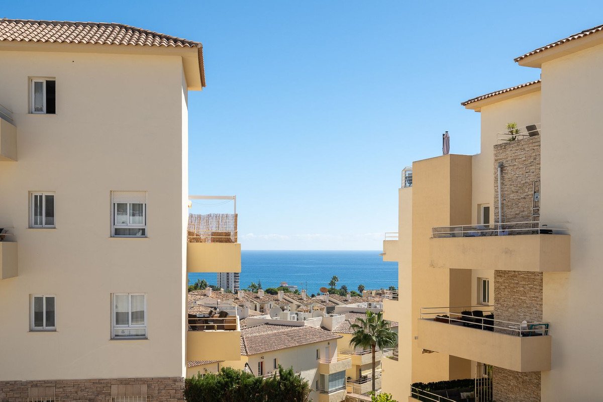 View of the sea from the balcony of apartments, with tiled roofs and buildings in the foreground under a clear blue sky.