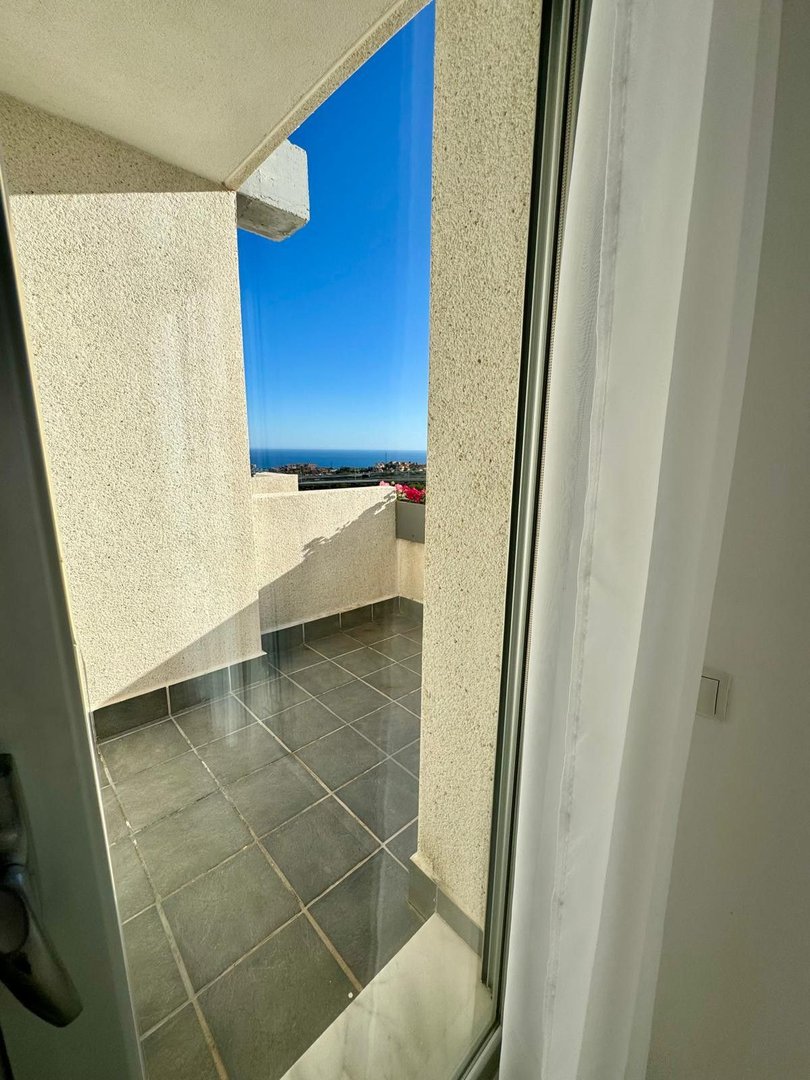 A balcony with a tiled floor opens to a view of the blue sky and the sea in the distance.